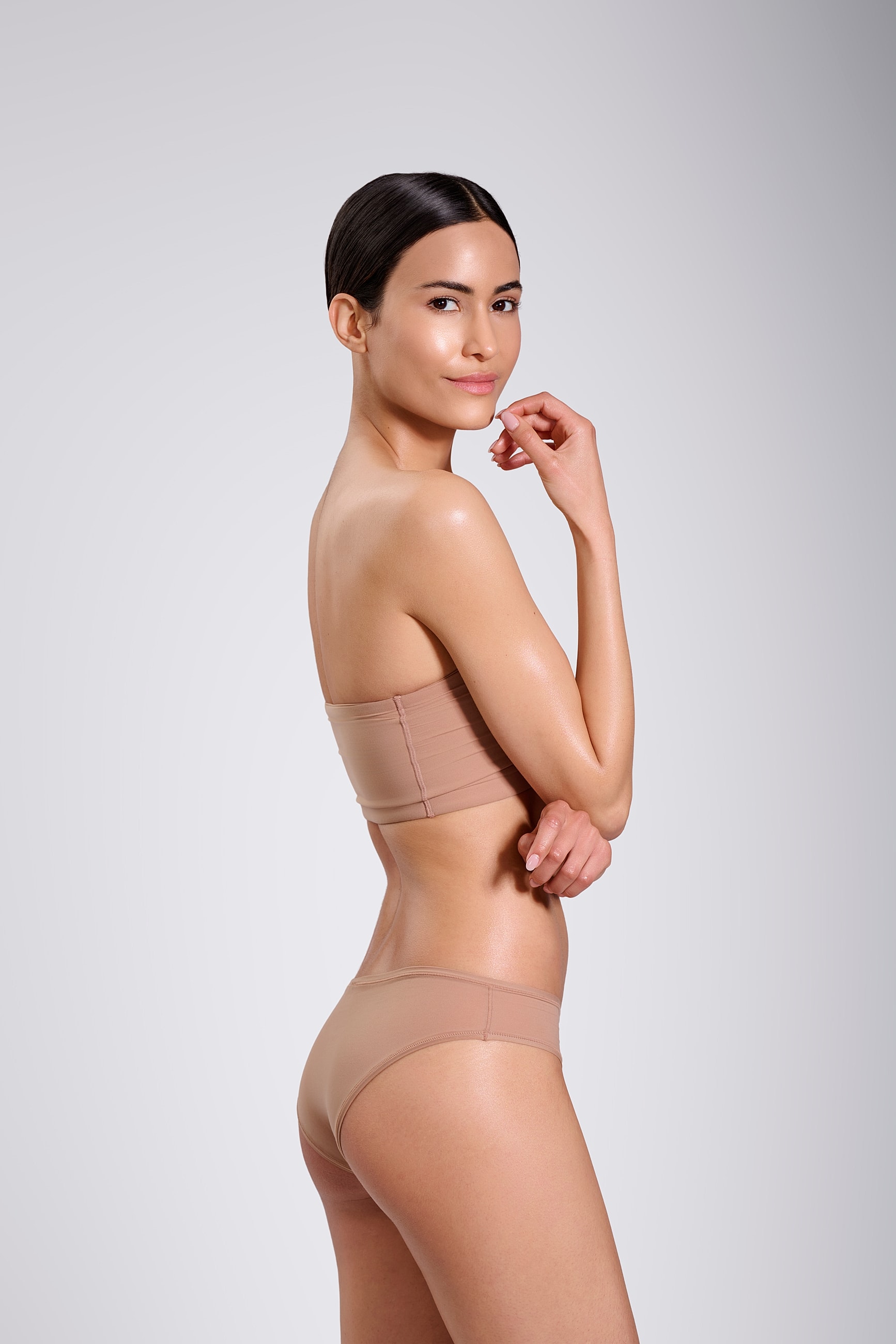 Model posing in nude-colored clothing against background.