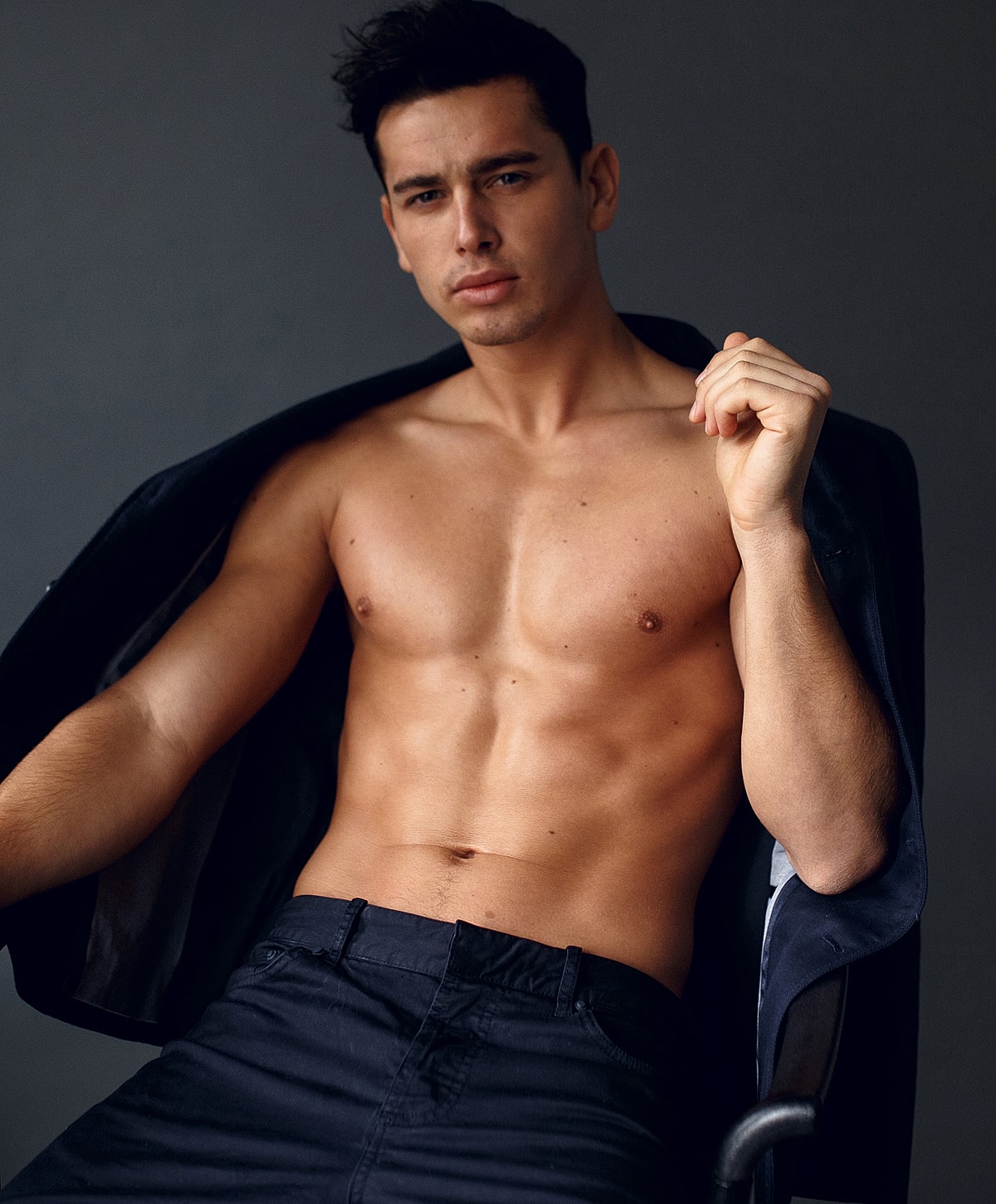 Shirtless man posing confidently in studio setting.