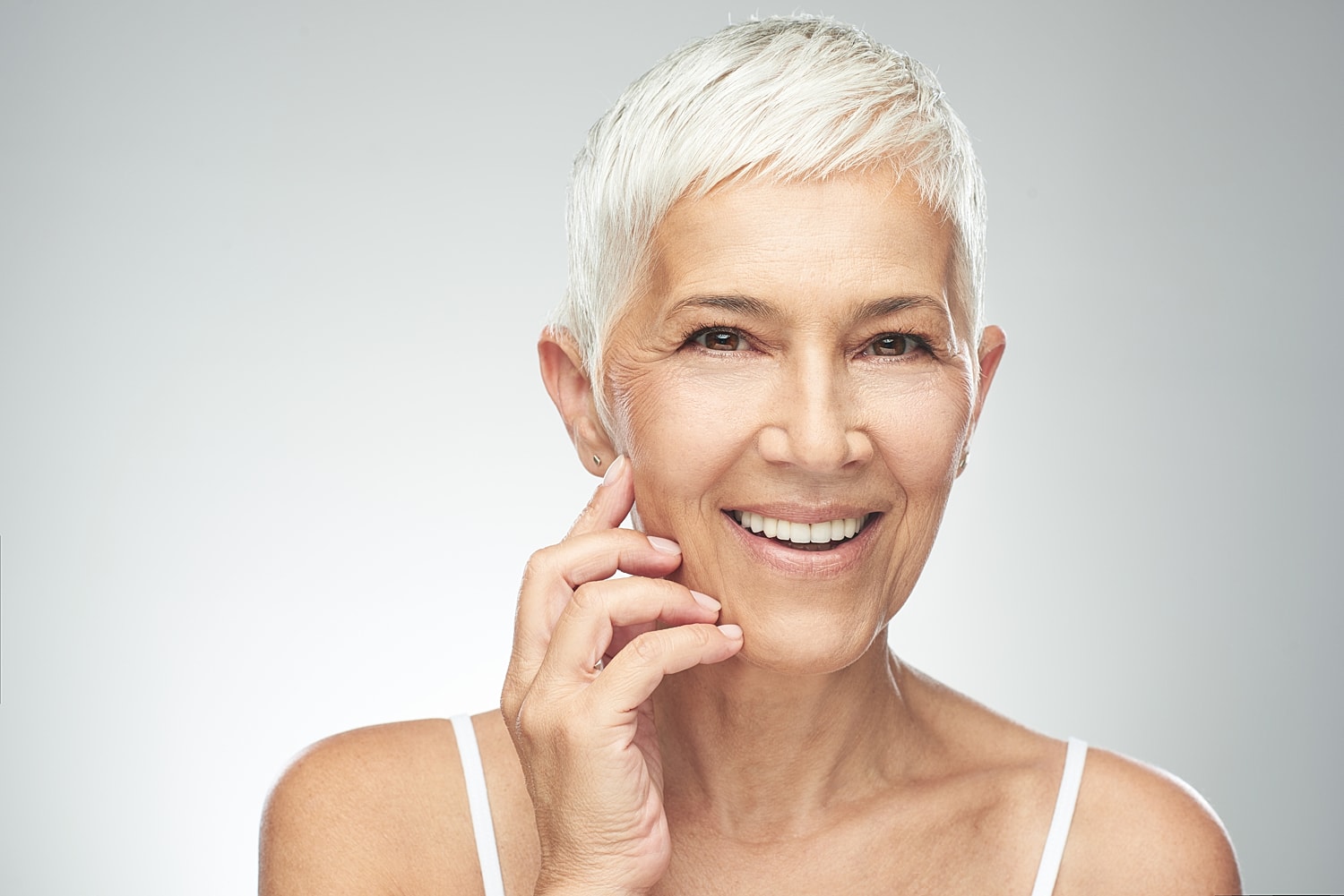Smiling older woman touching her face gently.