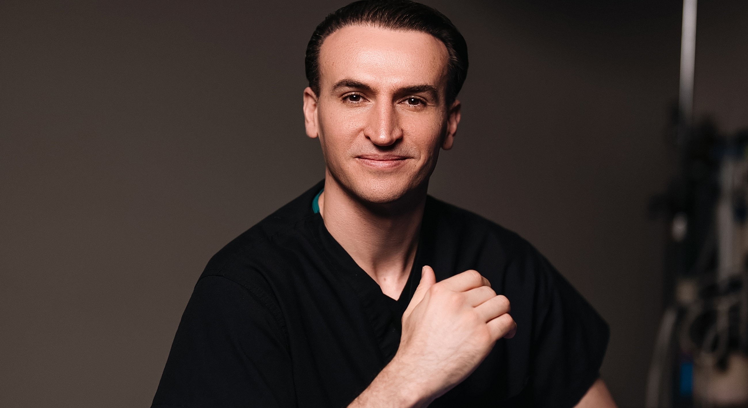 Male healthcare professional in black scrubs, smiling.