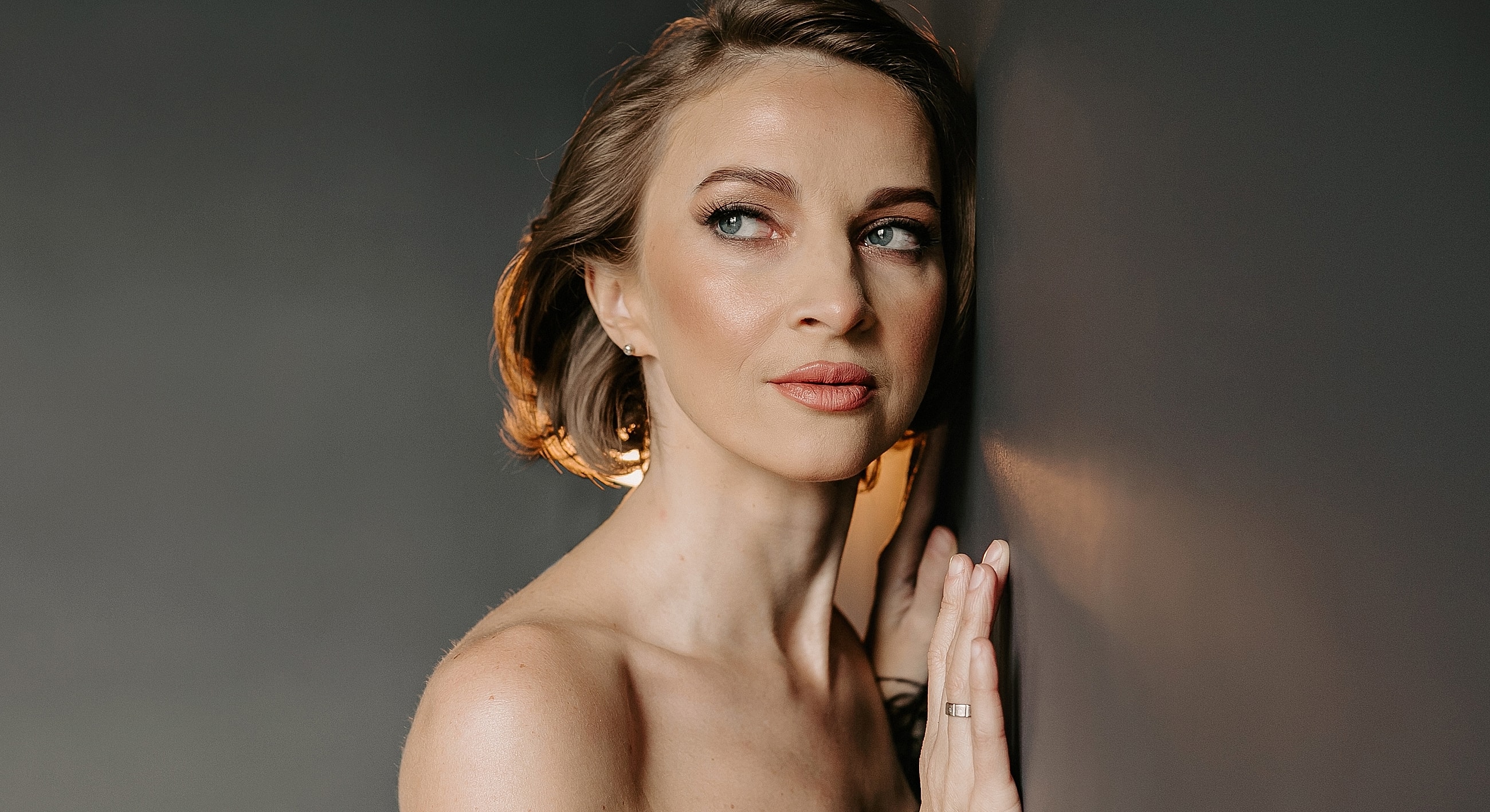 Woman posing against a dark wall, looking thoughtfully.