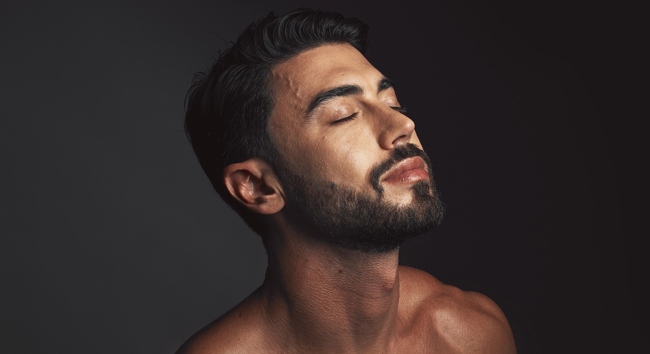 Man with closed eyes, serene expression, dark background.