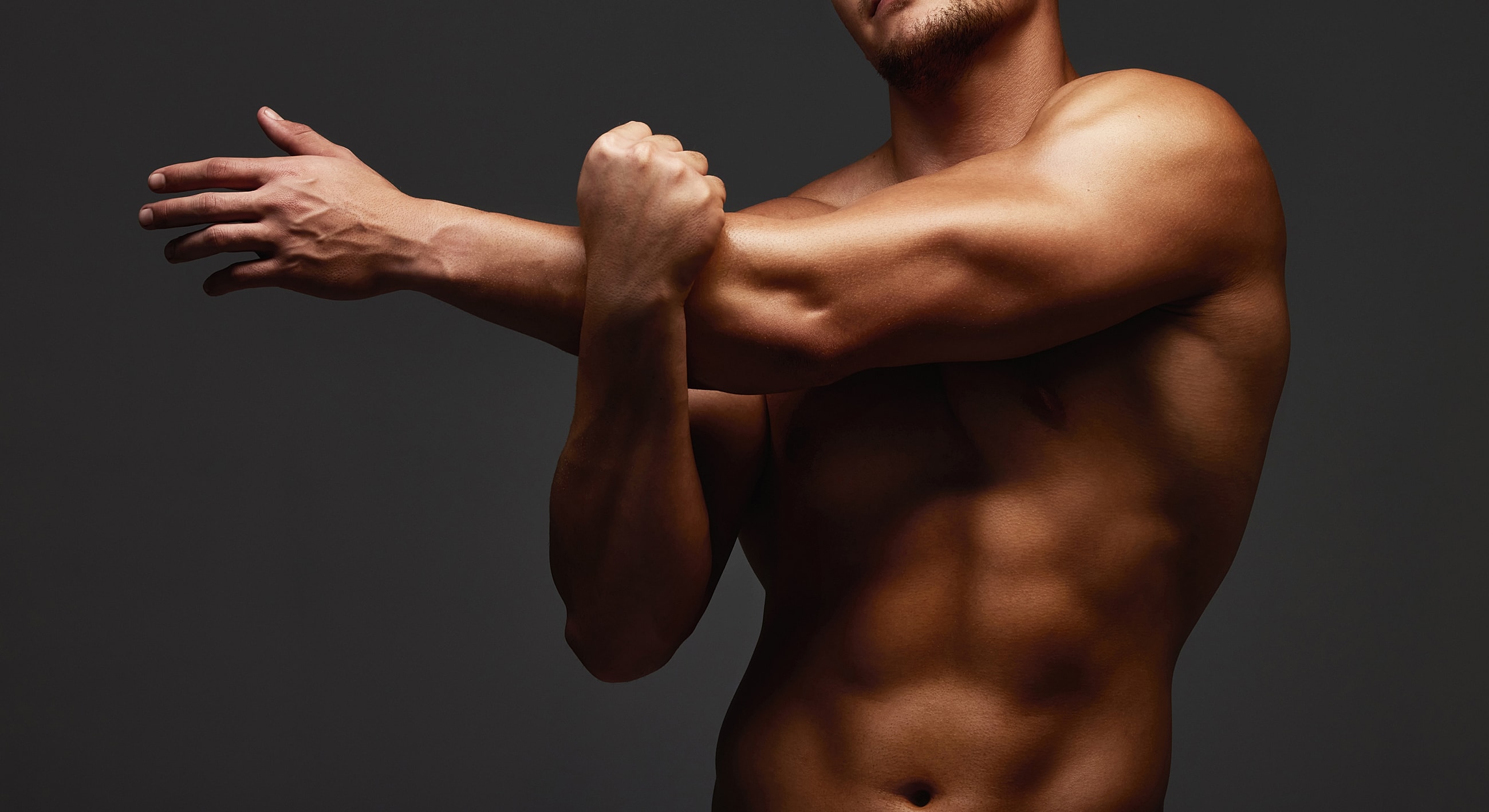Model stretching arms against dark background.