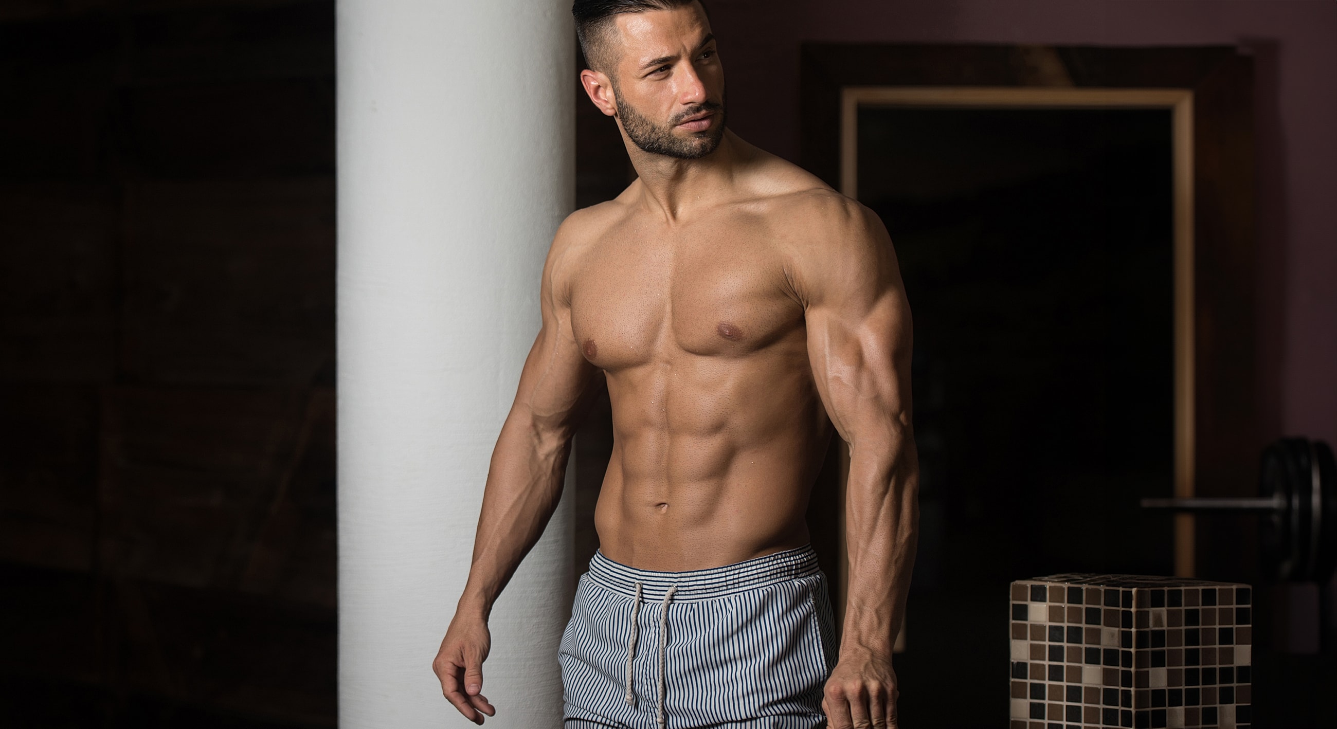 Muscular man posing near a column.