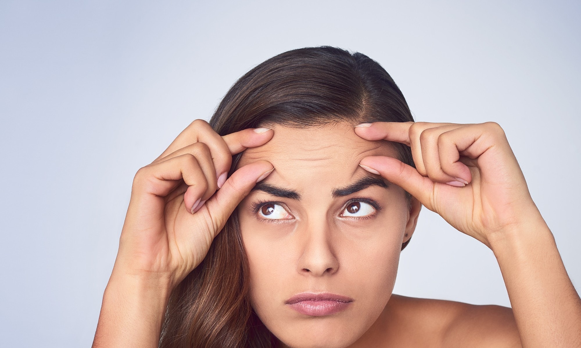 Woman examining her forehead wrinkles closely.